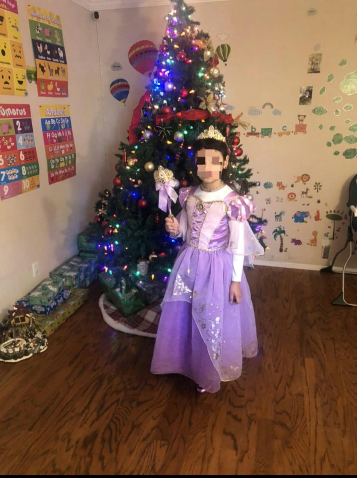 Child in a purple princess costume holding a wand next to a Christmas tree
