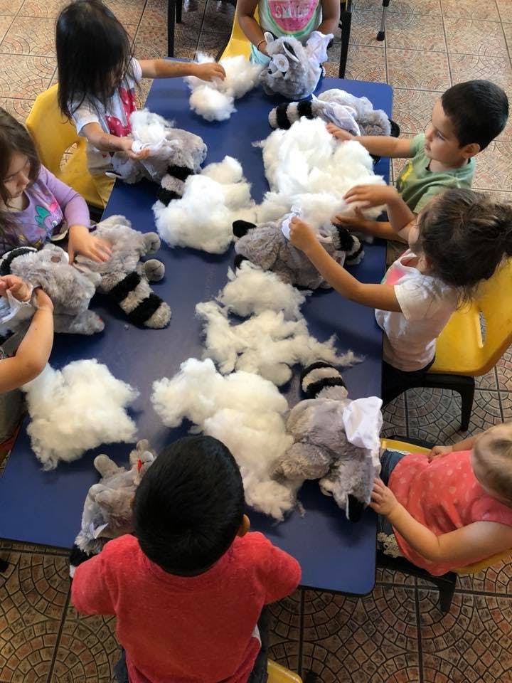 Children stuffing plush toys with white fiber filling at a table