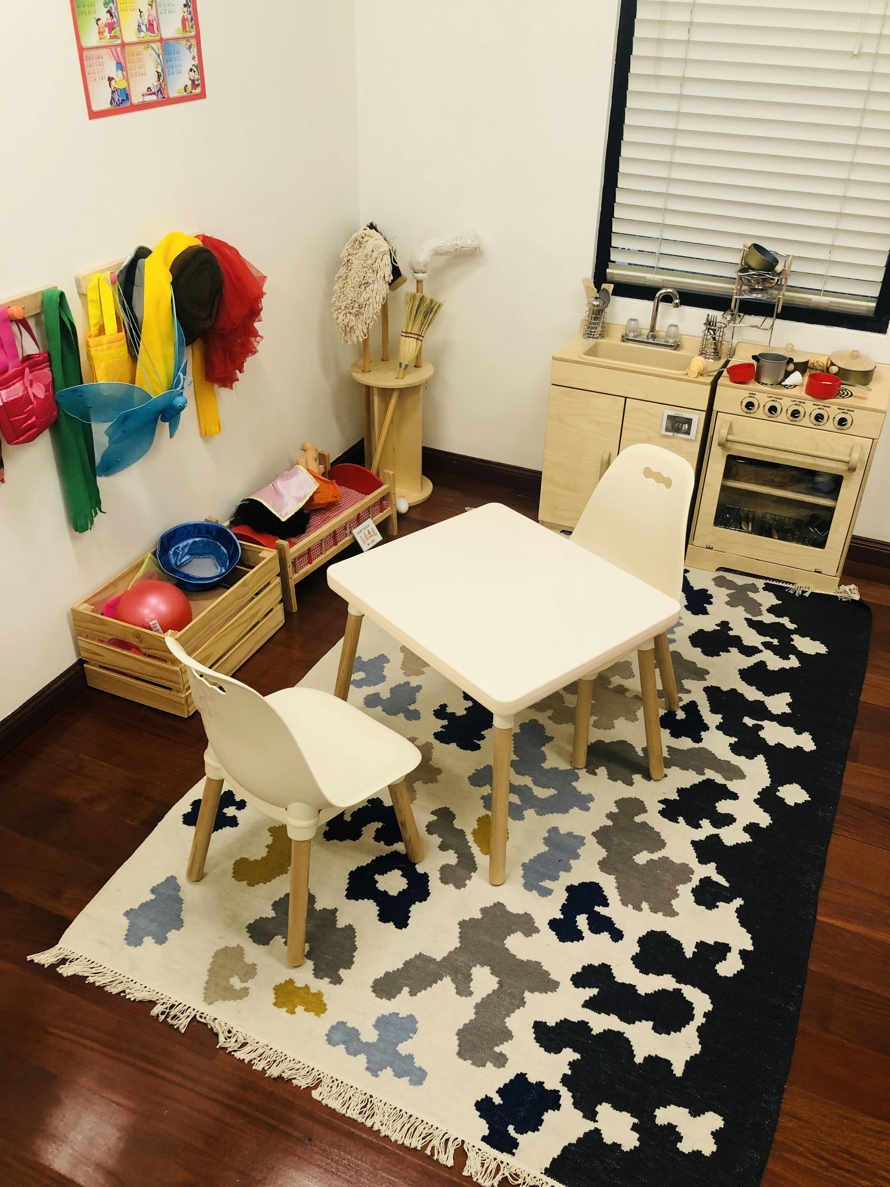 A children's play area with a small table and chairs, a play kitchen, and dress-up clothes