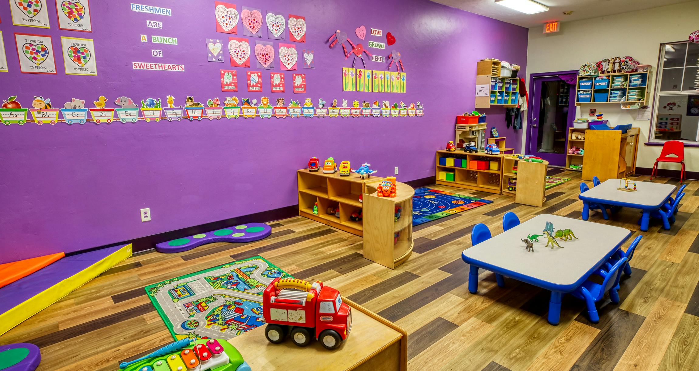 Colorful classroom with small tables and chairs, shelves with toys, and decorations on the wall