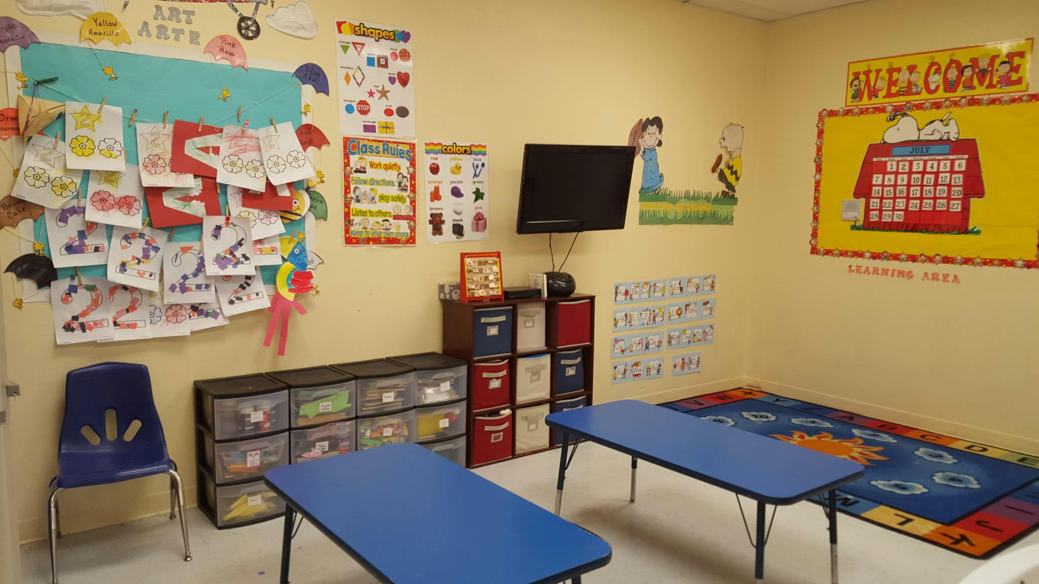 Classroom with children's artwork on the wall and small blue tables