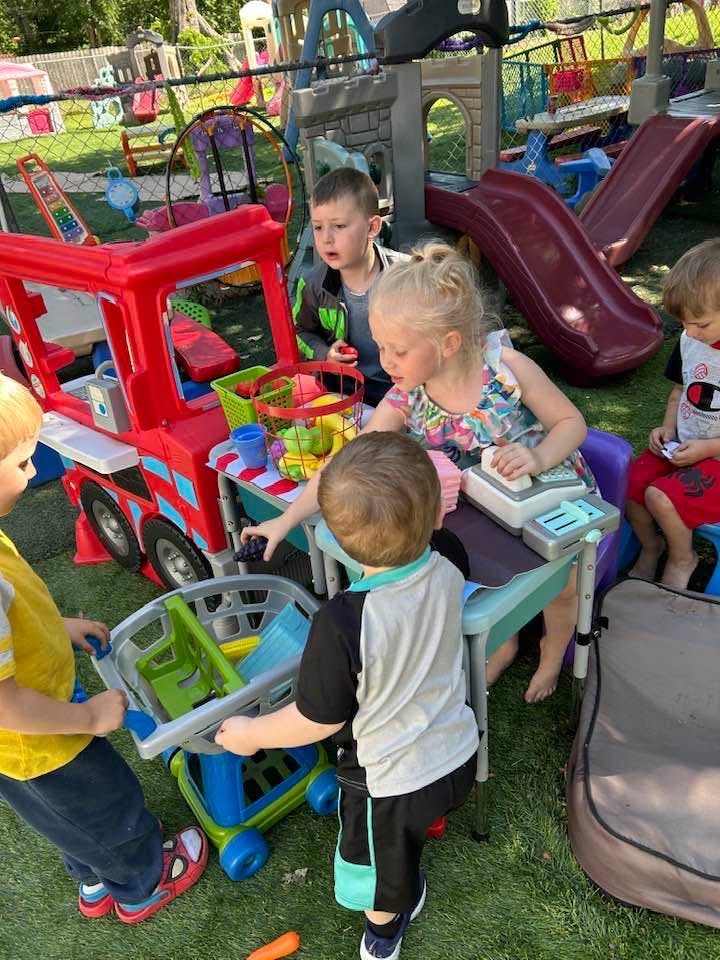 Children playing with a toy store and grocery cart in a backyard