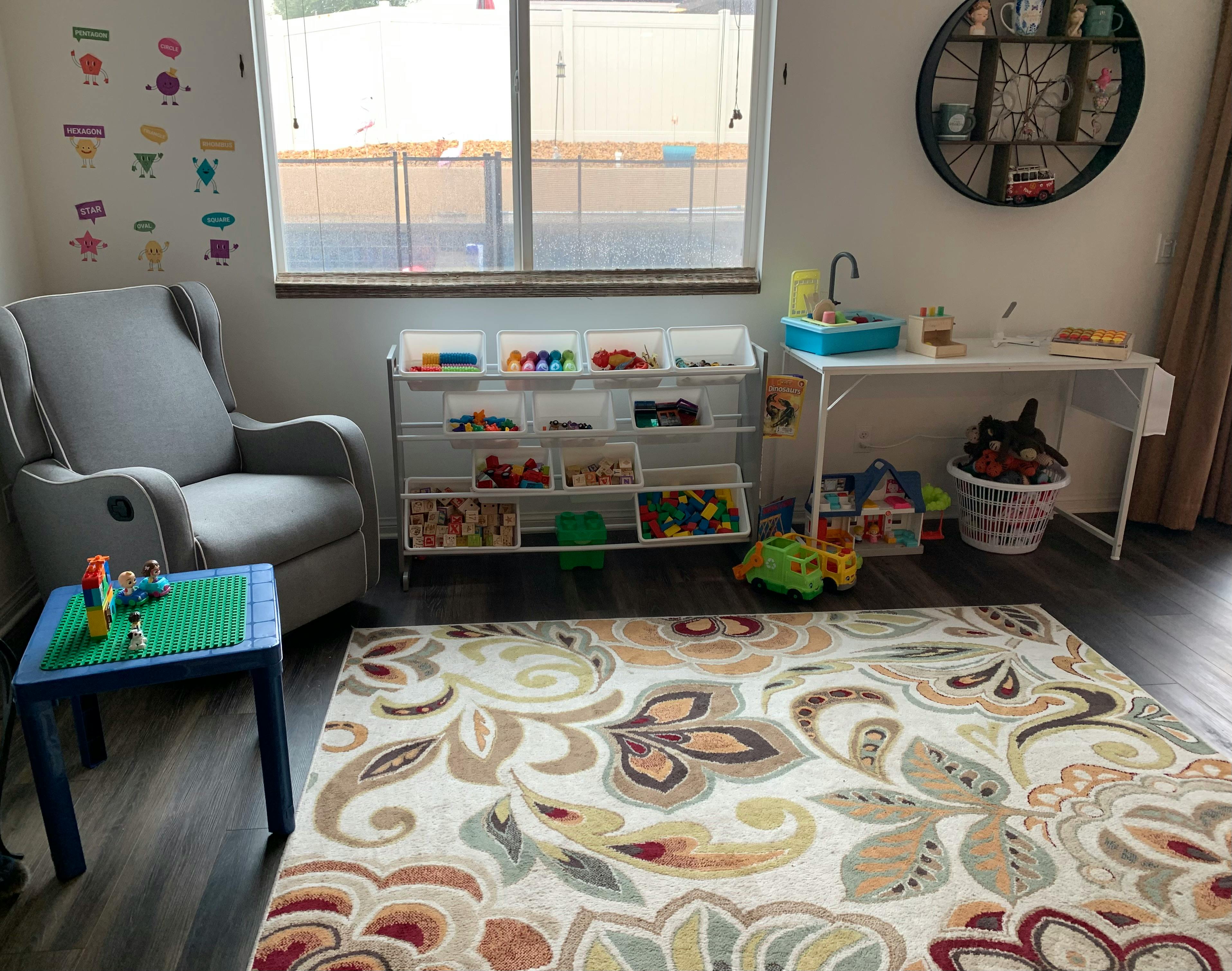 Playroom with a gray armchair, toy storage, and a patterned rug