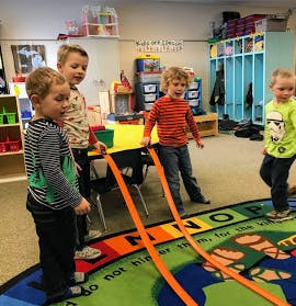 Four children playing with orange tracks on a rug in a classroom