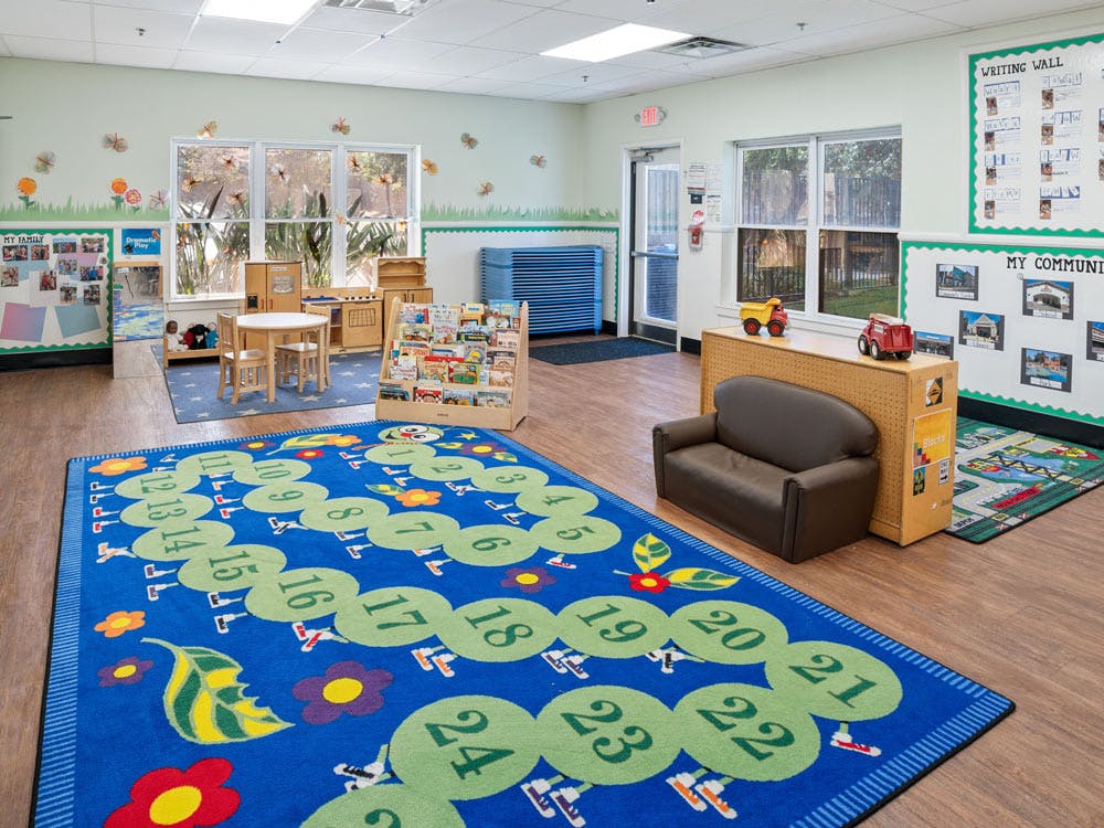 An empty classroom with a counting rug, small tables, and bookshelves