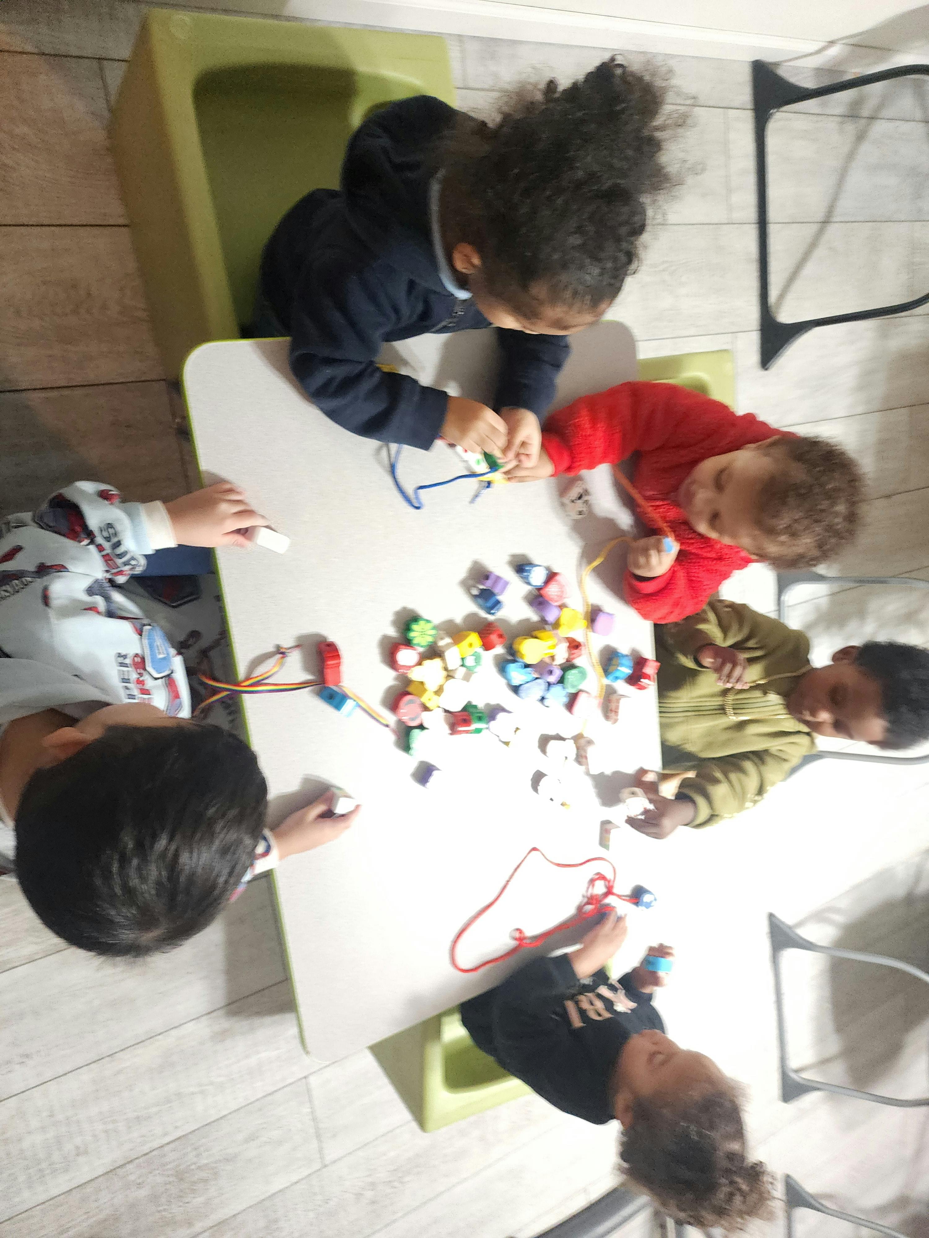 Five children playing with beads and strings around a table