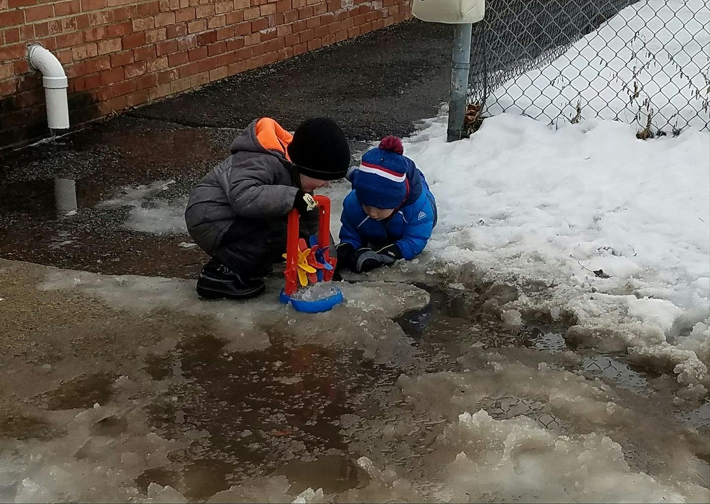 Two children playing in melting snow and ice