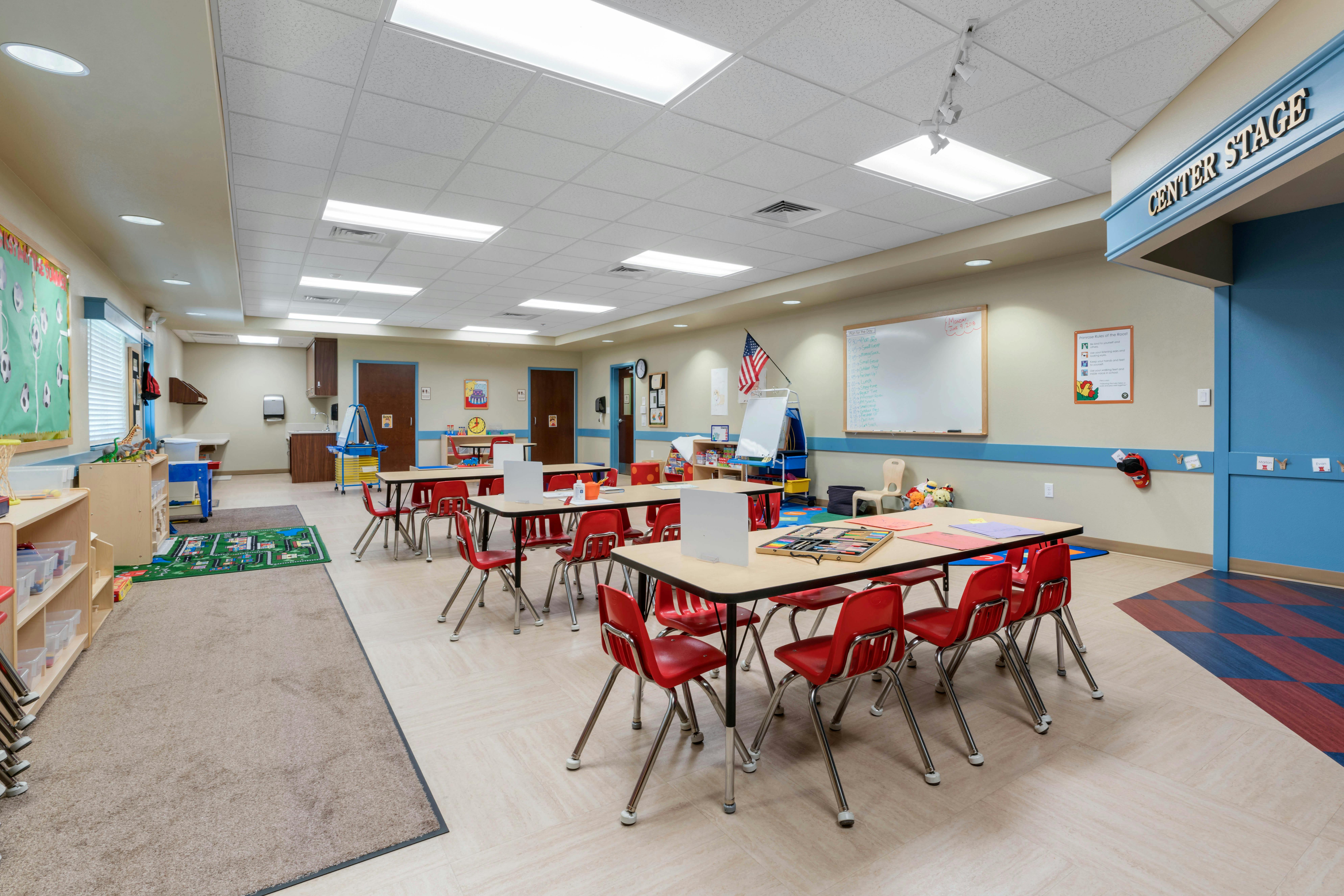 Classroom with small tables, red chairs, and a 'Center Stage' sign above a door
