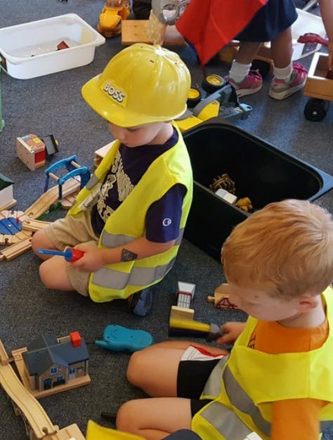 Children playing with toy construction tools and wooden train tracks