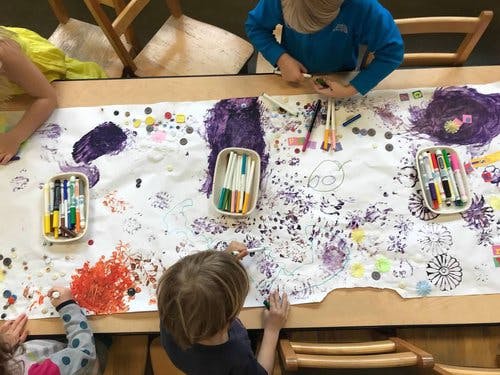 Children drawing on a large sheet of paper with markers