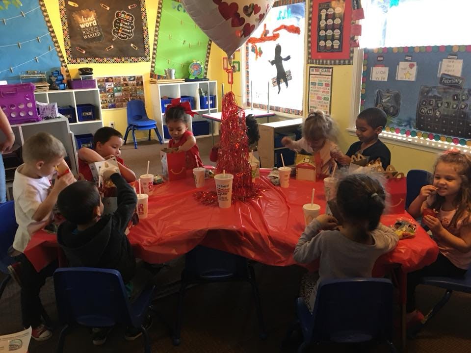 Children sitting around a table with a red tablecloth in a classroom