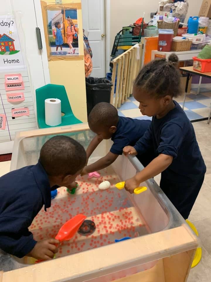 Three children playing with toys in a sensory bin