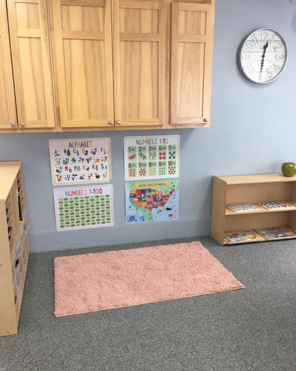 Classroom with wooden cabinets, educational posters, and a pink rug