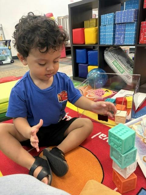 Child sitting on a colorful floor mat and stacking plastic building blocks