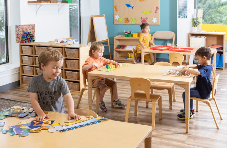 Children playing with puzzles and toys at tables in a classroom