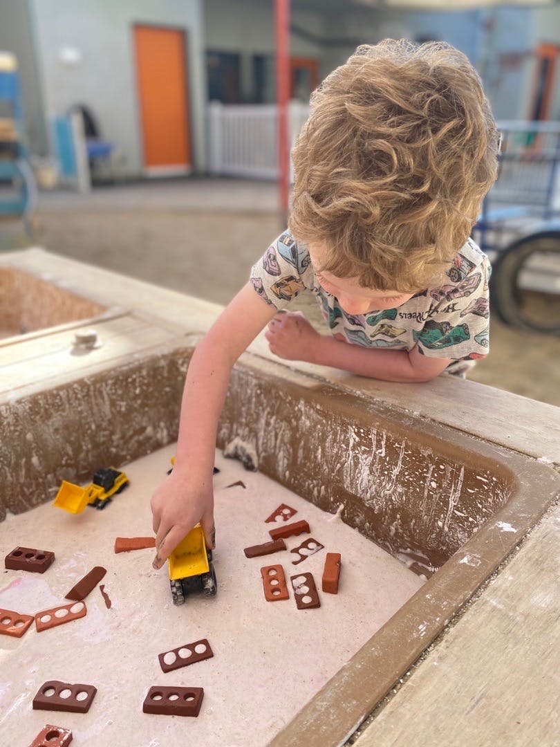 Child playing with toy dump trucks and toy bricks in a sensory bin