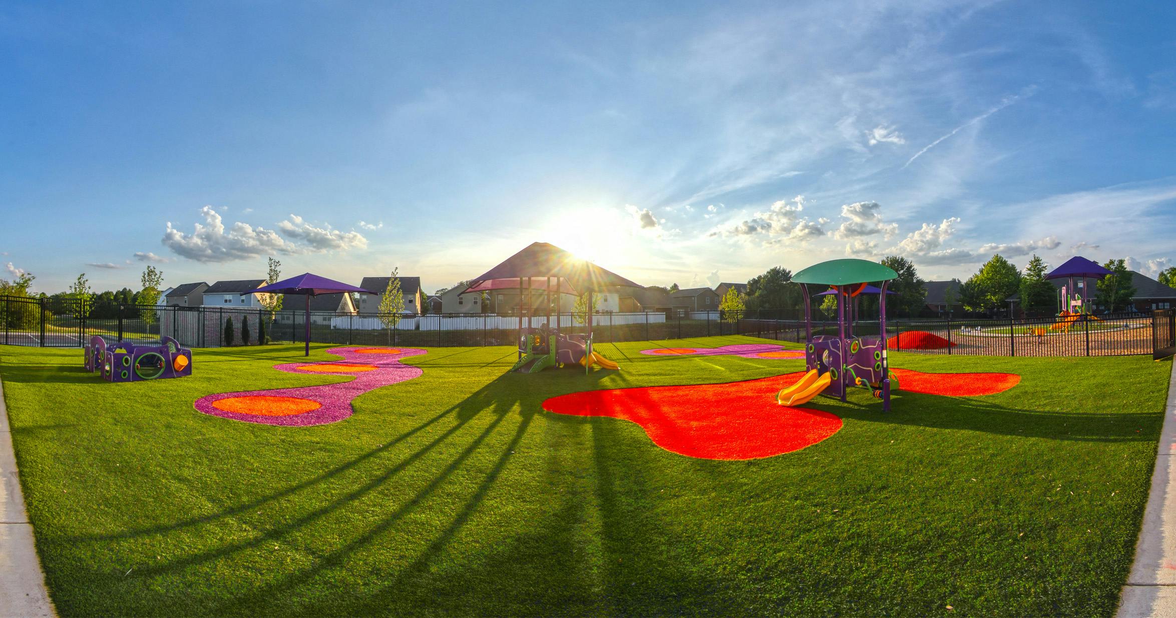 Playground with various colorful equipment on artificial grass, sun in background
