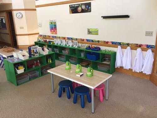 Classroom with green shelves, small tables, and stools