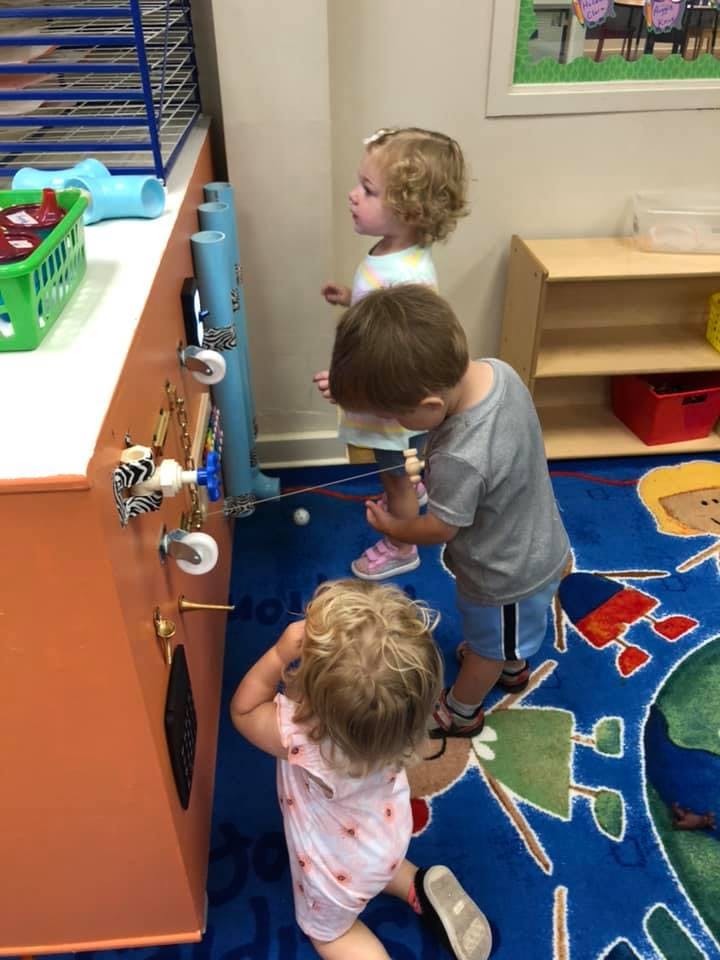 Three children playing with a busy board in a classroom