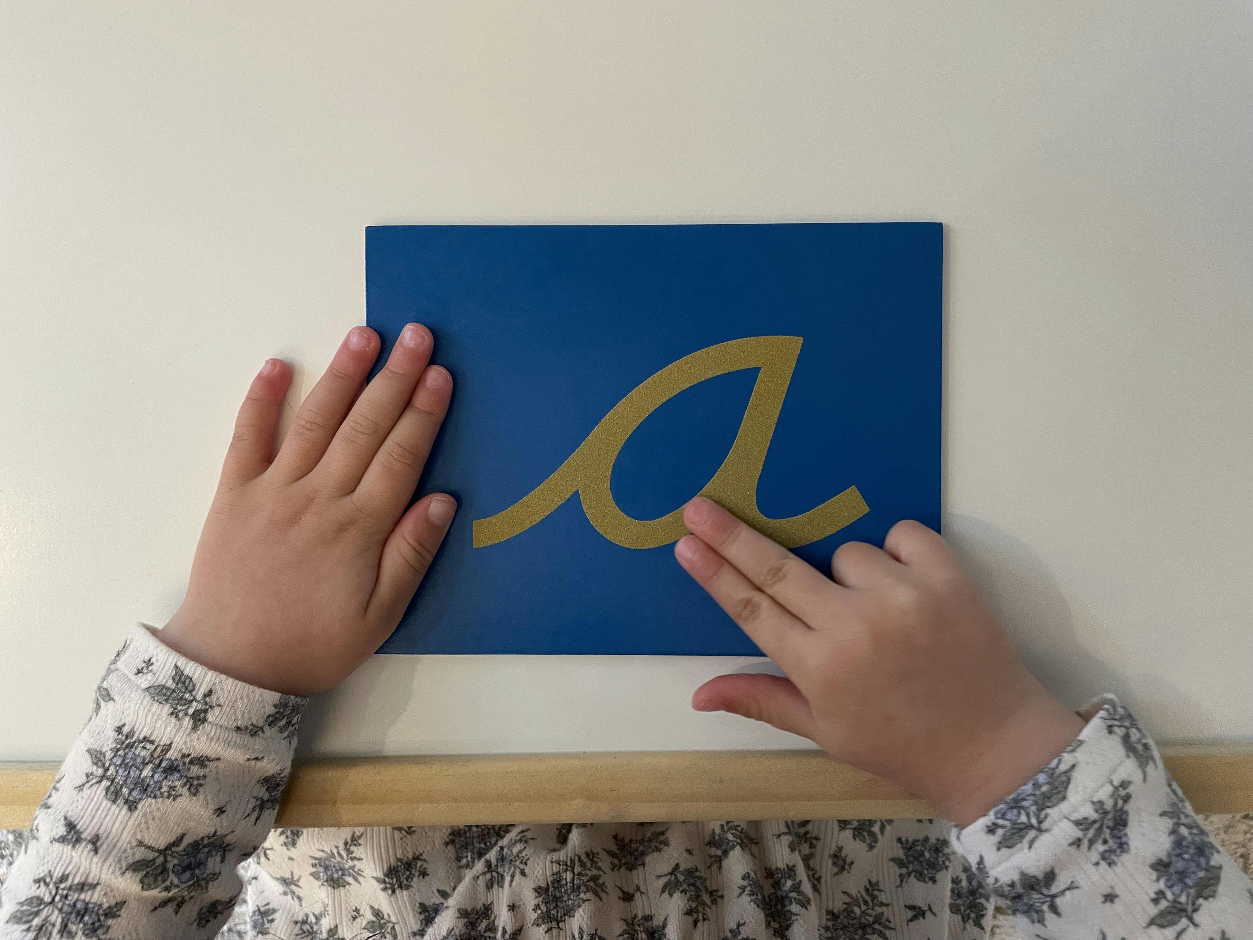 Child tracing the letter a on a textured blue card