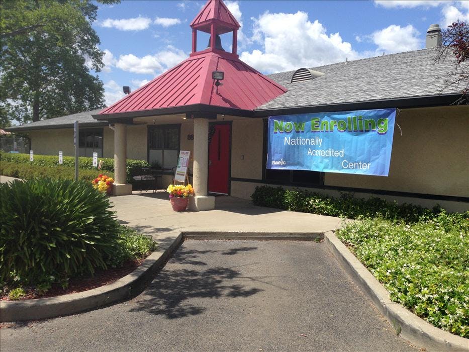Building with a red roof, red door, and a blue banner that reads "Now Enrolling"
