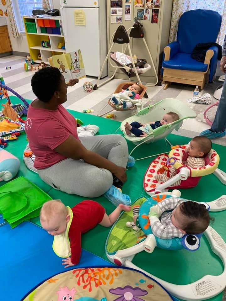 Person sitting on floor with multiple babies in a play area