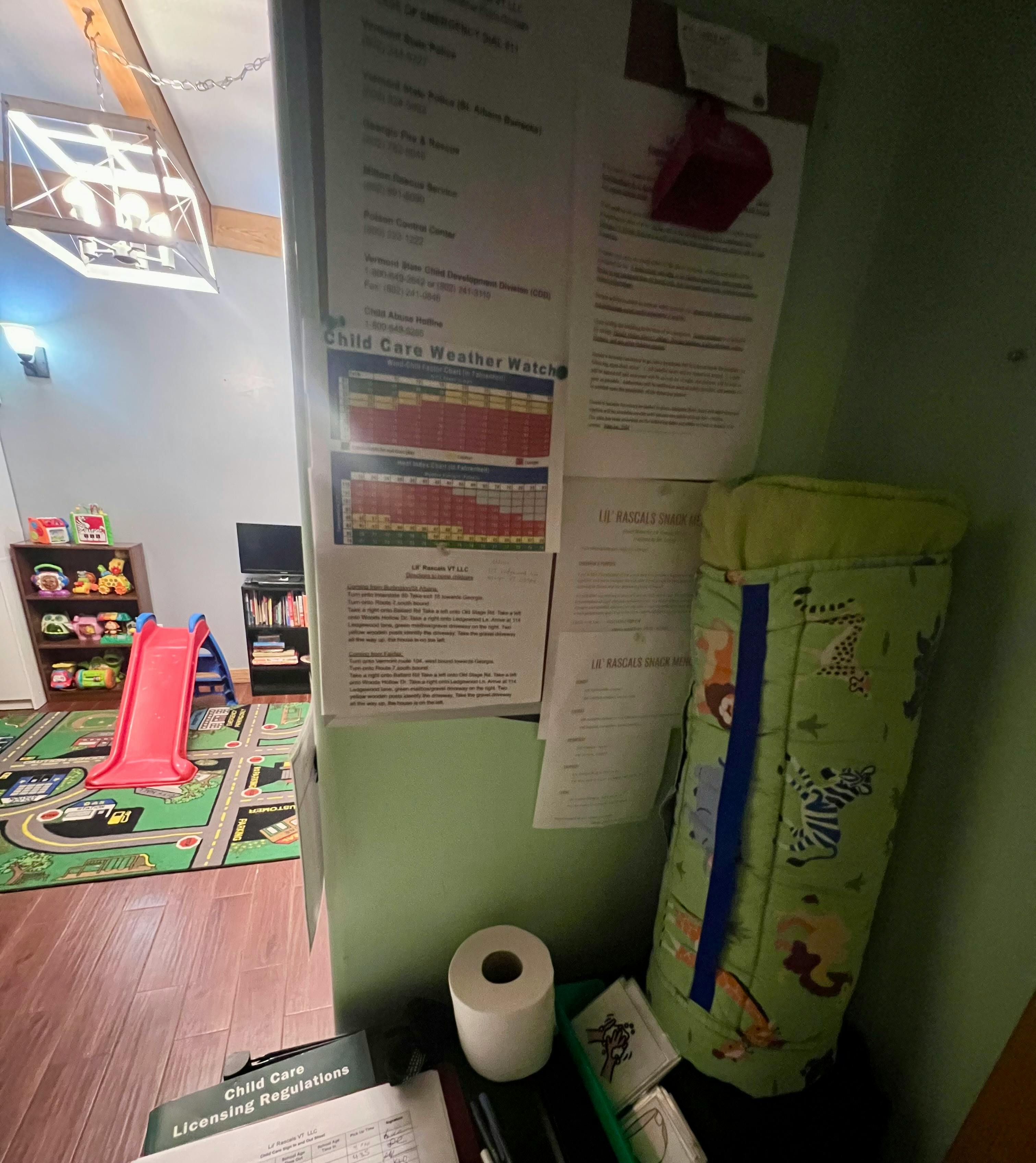 Child care room with a red slide, toy shelf, and papers on a wall