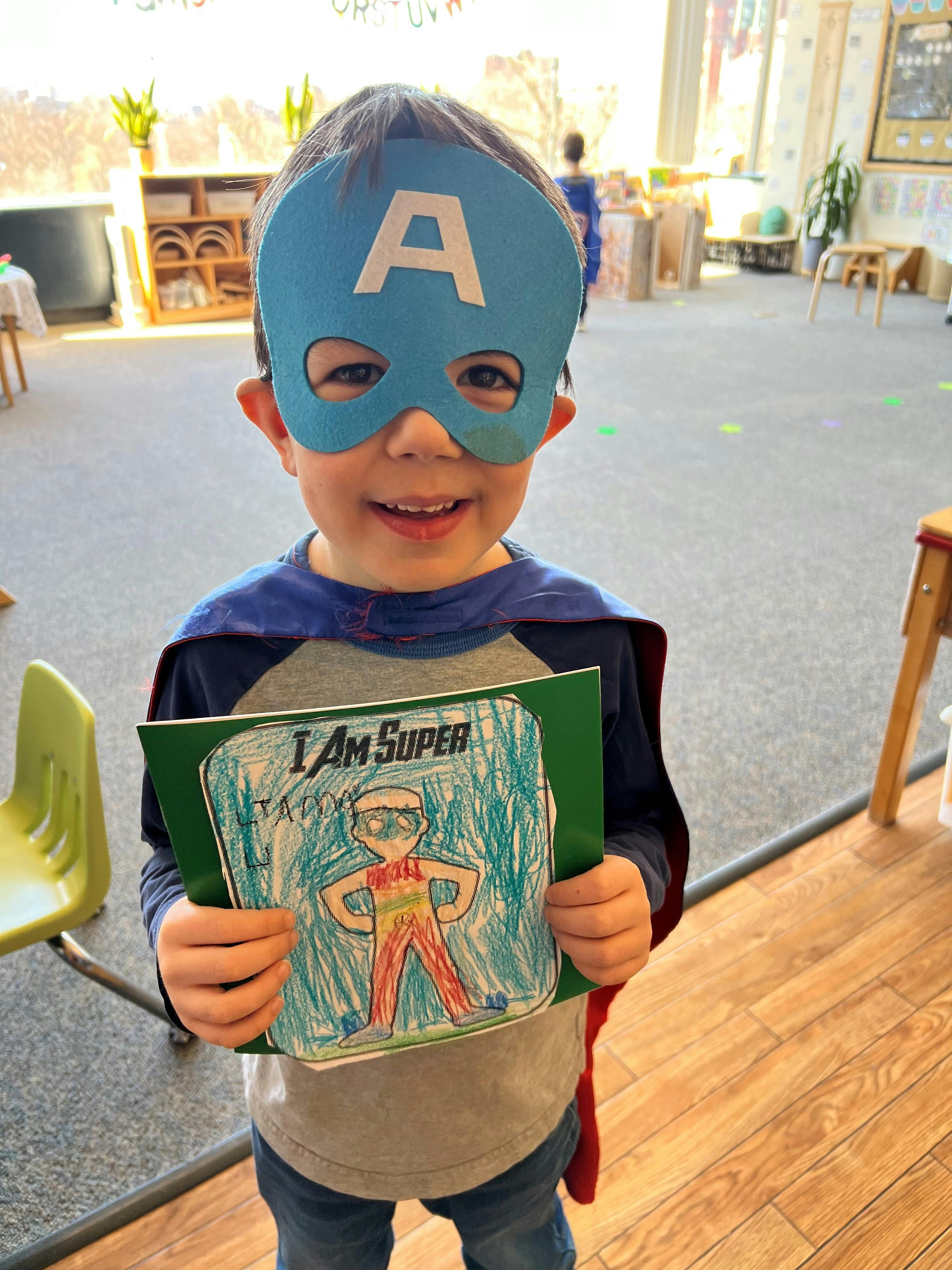 Child in a superhero mask and cape holding a drawing that says "I Am Super"