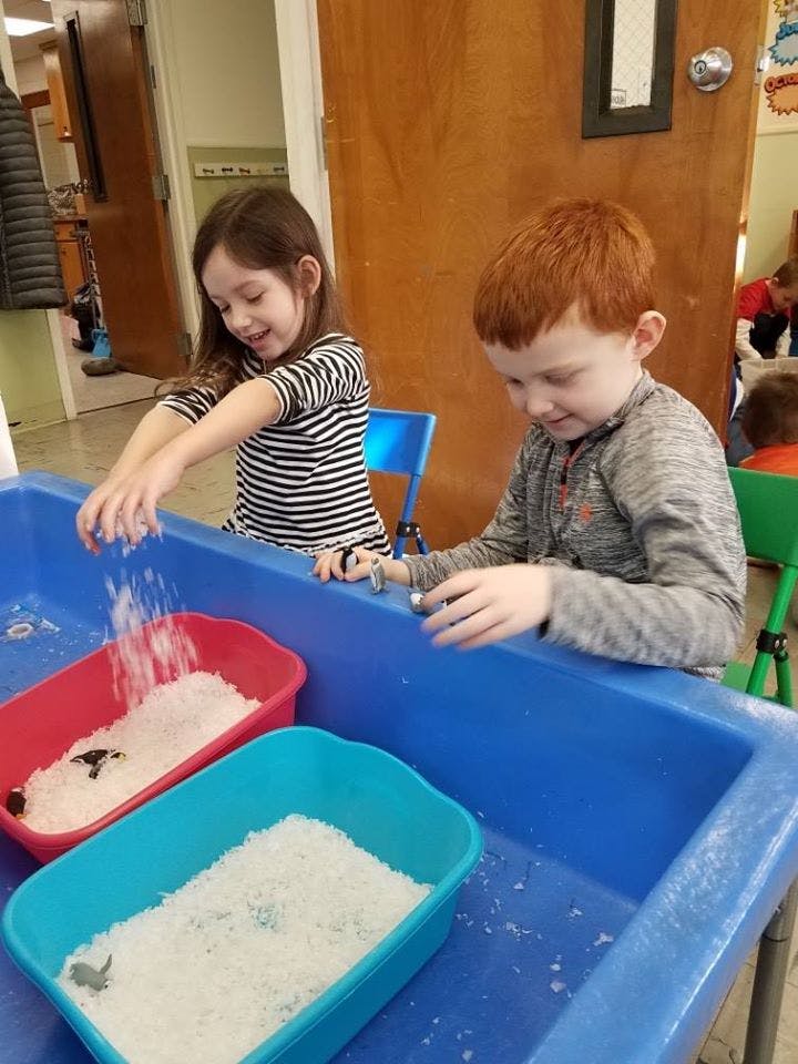 Two children playing with rice in a blue sensory bin
