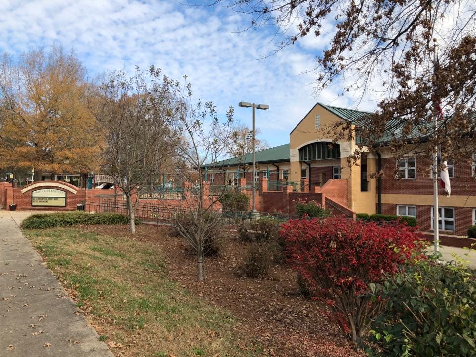 Building with brick and tan facade, green roof, and red bushes in front