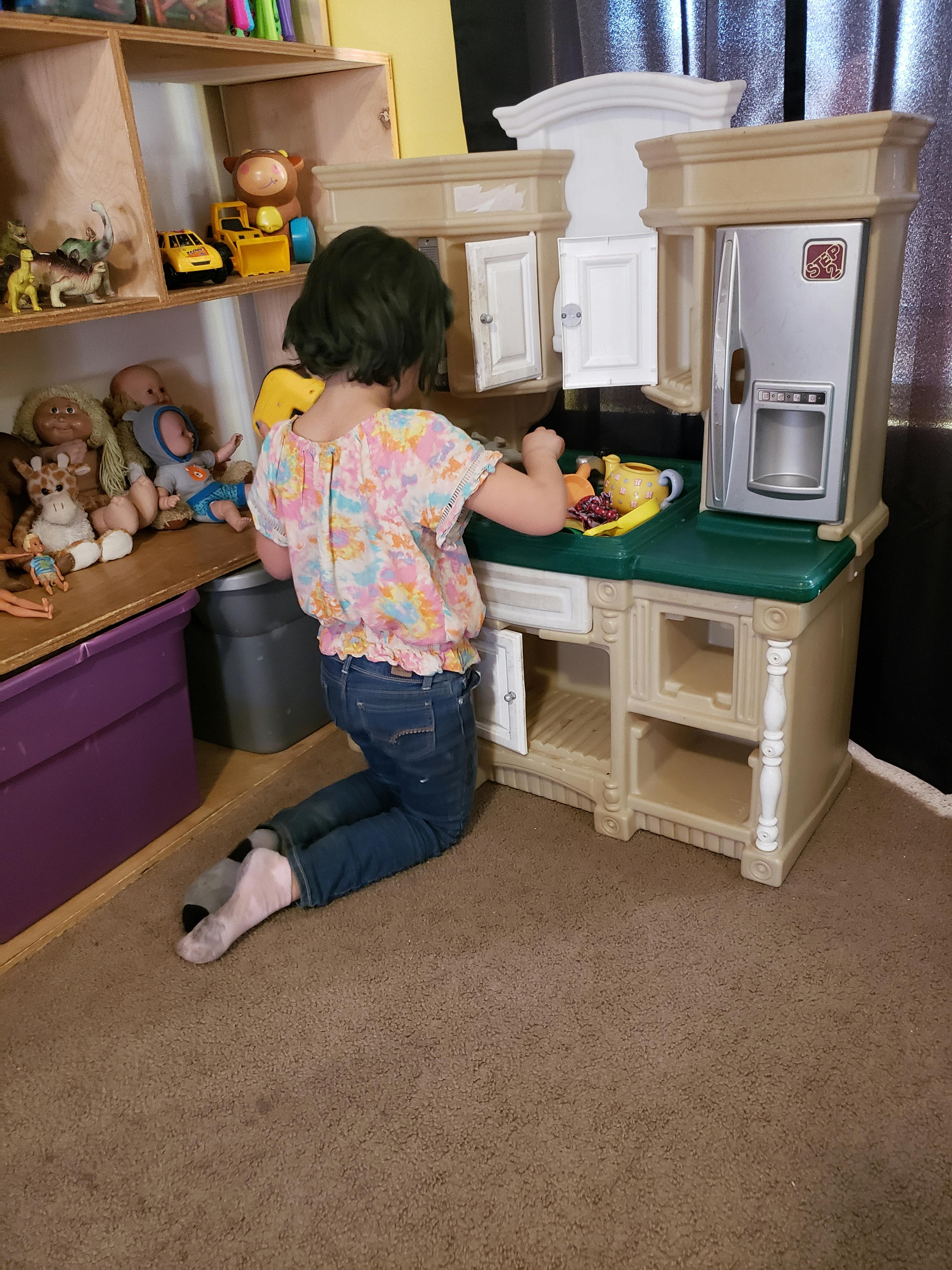 Child kneeling and playing with a toy kitchen set