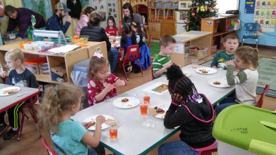 Children and adults eating at tables in a classroom