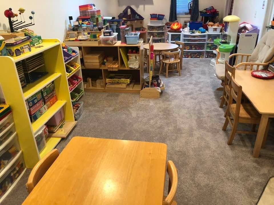 Classroom with small tables and chairs, shelves with books and toys