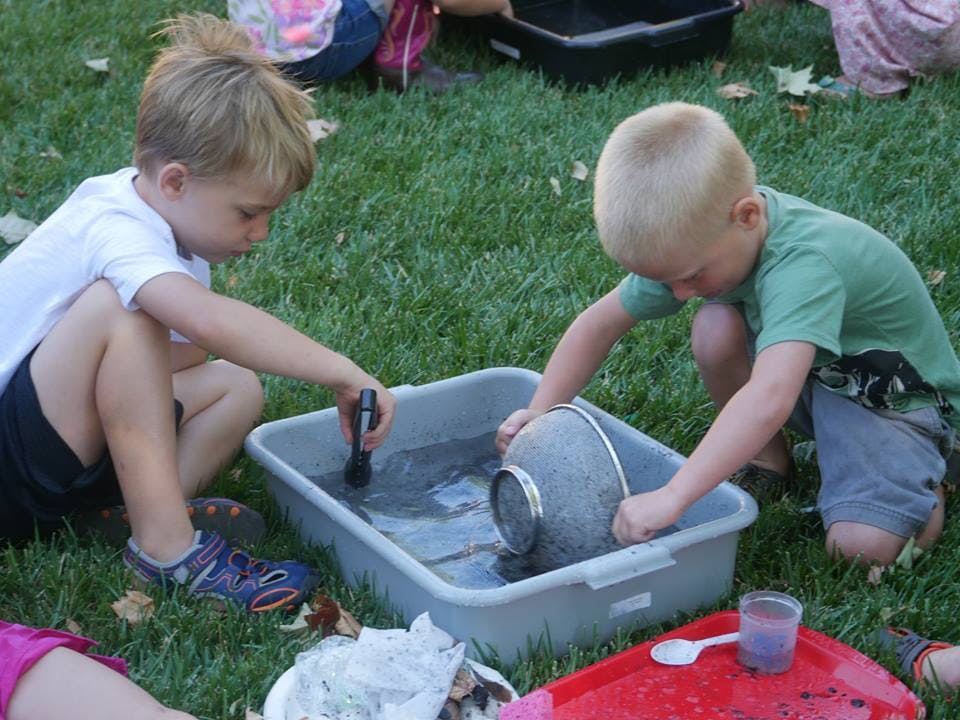 Two children playing with water in a bin on grass