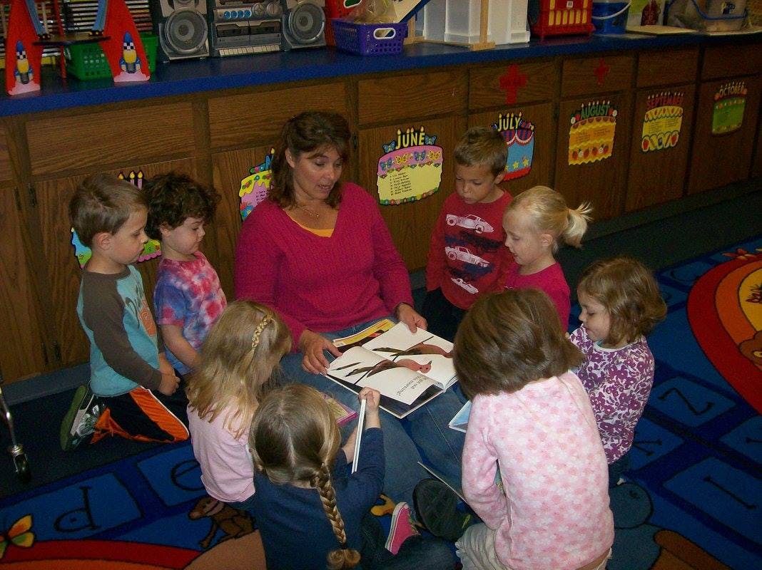 Adult reading a book to a group of children in a classroom