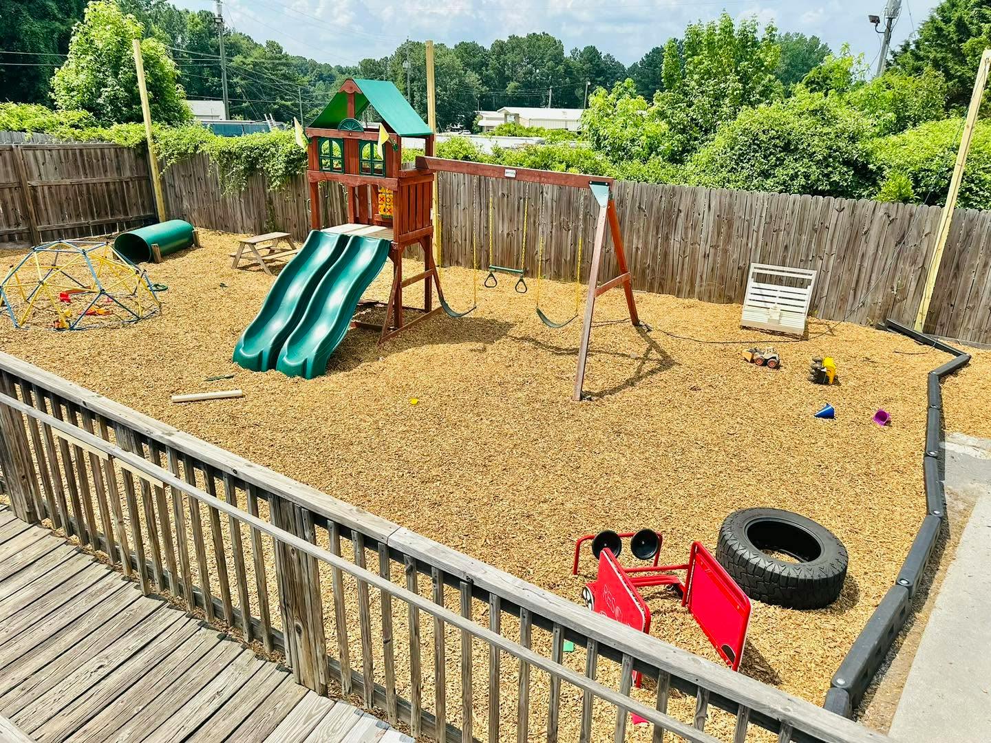Wooden playset with slides, swings, and a climbing dome in a fenced yard