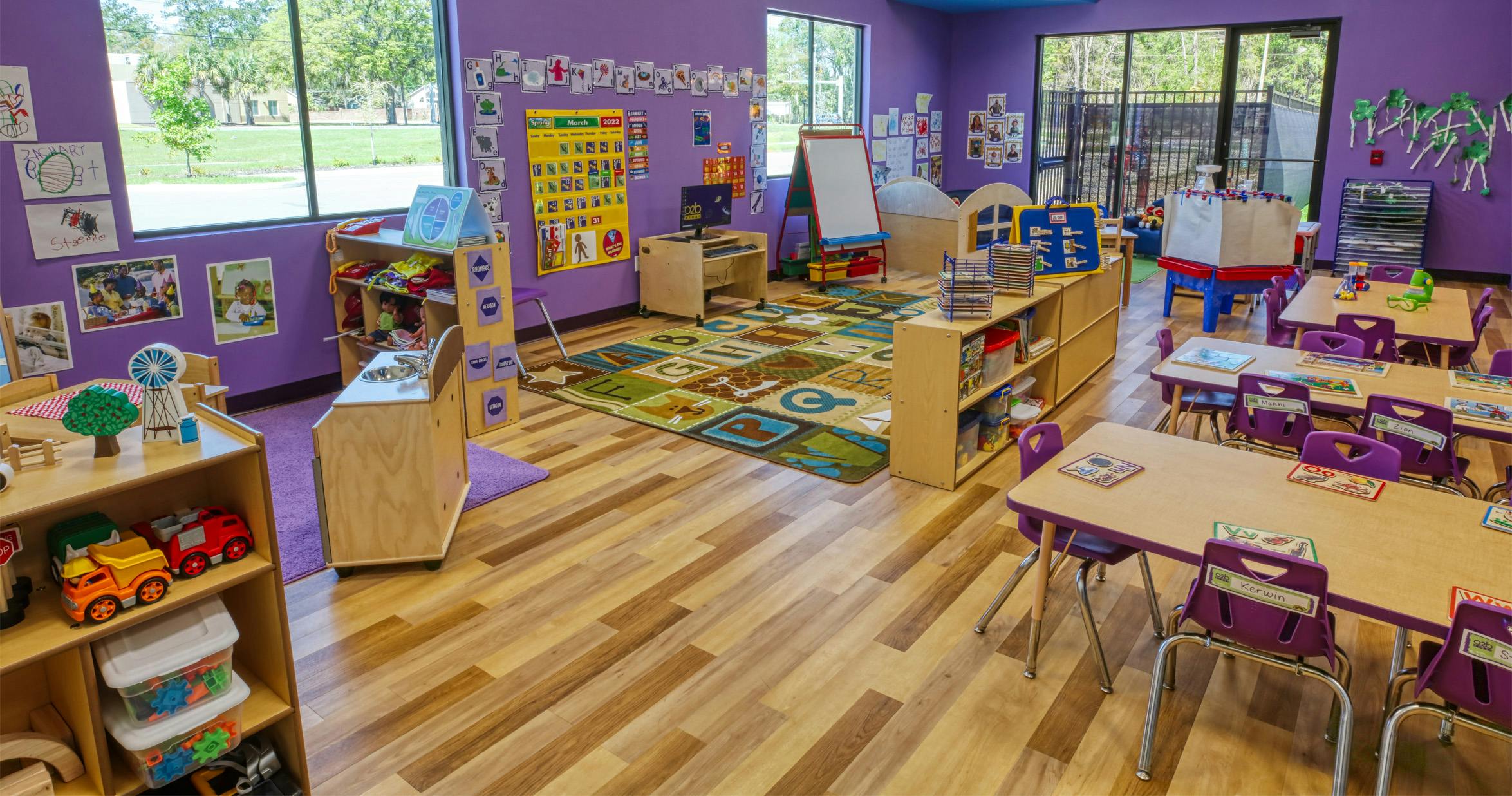A colorful empty classroom with purple walls, small tables, and learning stations
