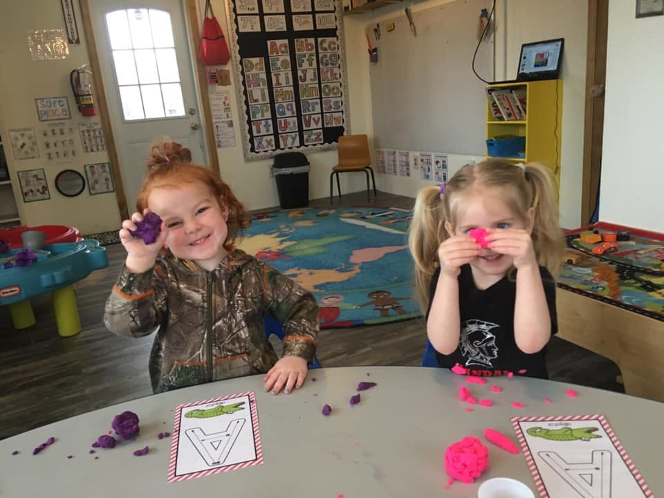 Two children playing with modeling clay at a table in a classroom