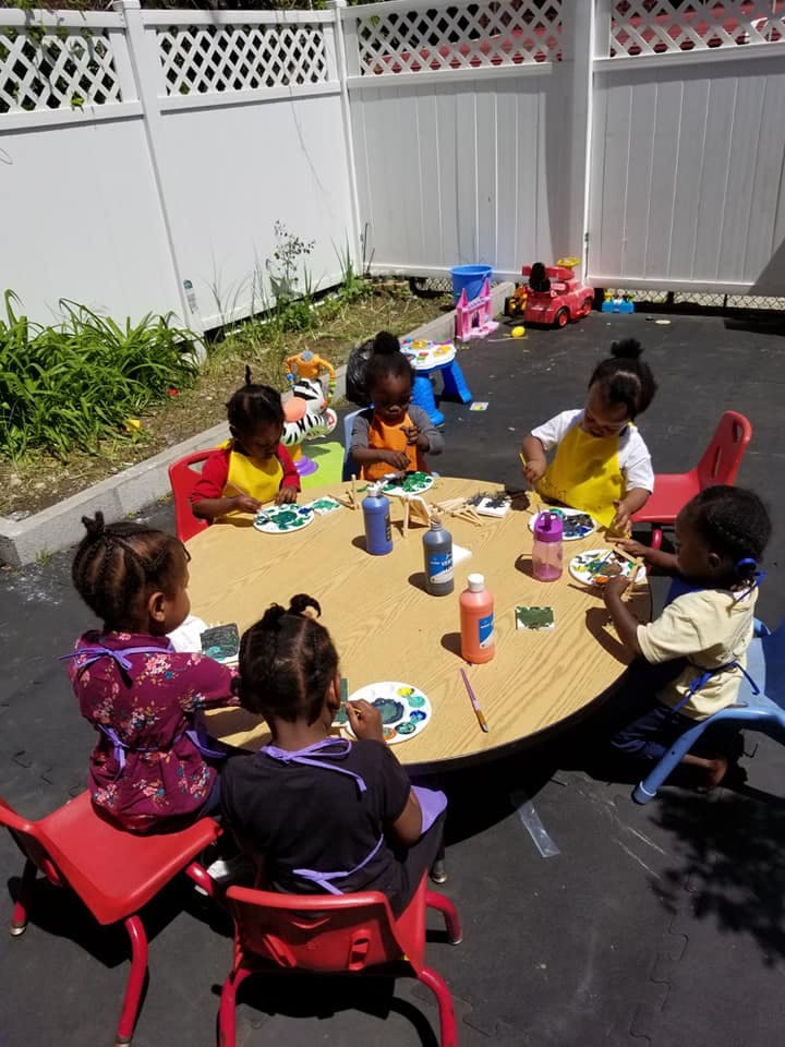 Children painting at a round table outdoors
