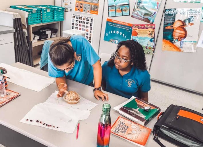 Two people looking at a small object on a table in a classroom