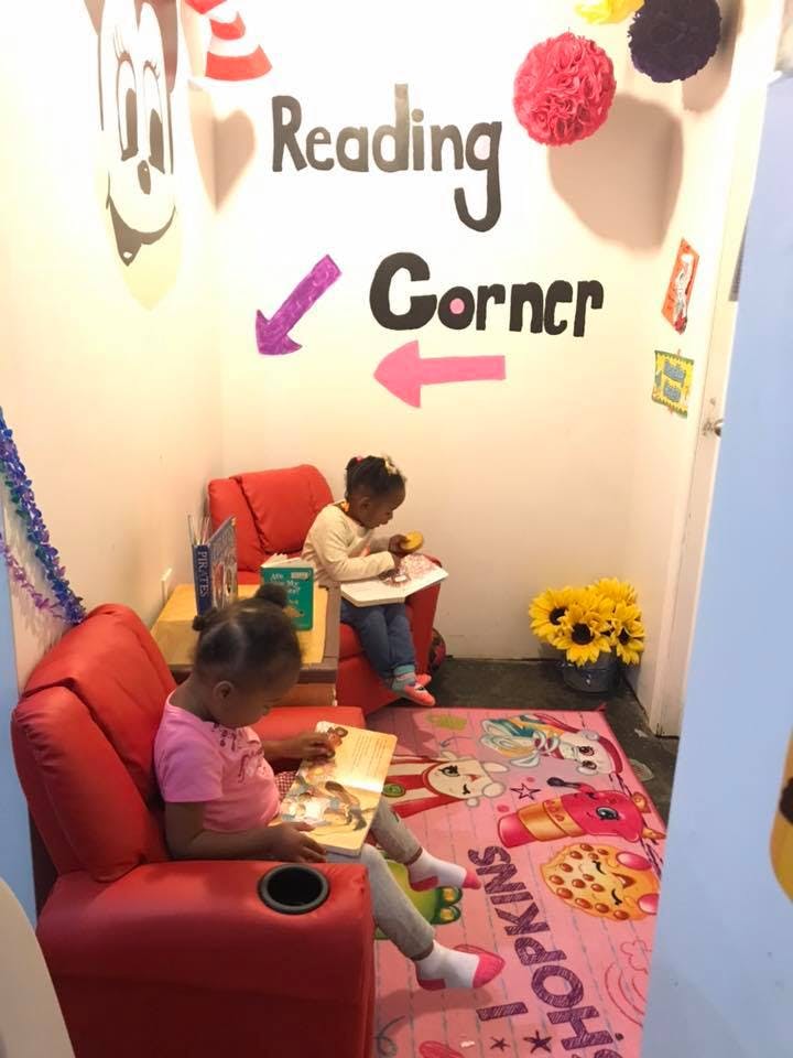 Two children reading books in a "Reading Corner" with red chairs