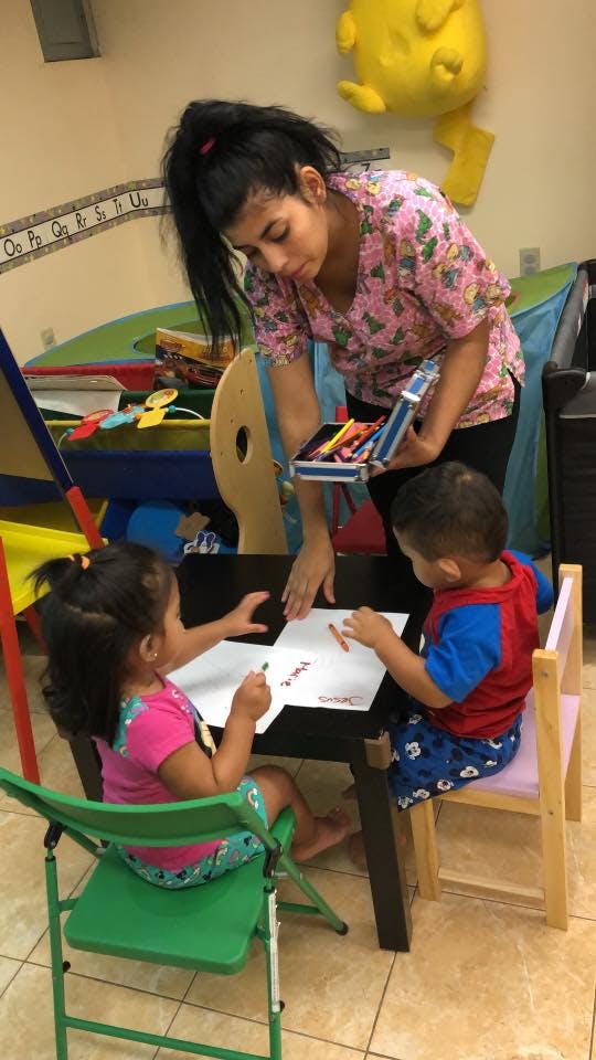 Person holding crayons while two children draw at a table