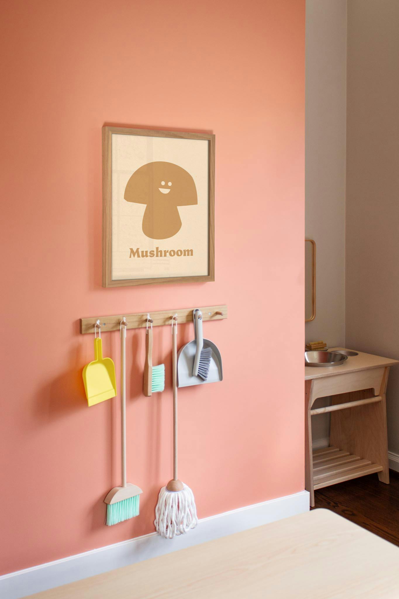 Mushroom art print above a rack with a broom, mop, and dustpans