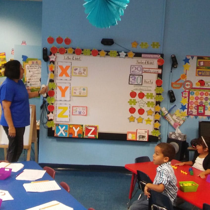 Person pointing at a whiteboard with letters and numbers in a classroom