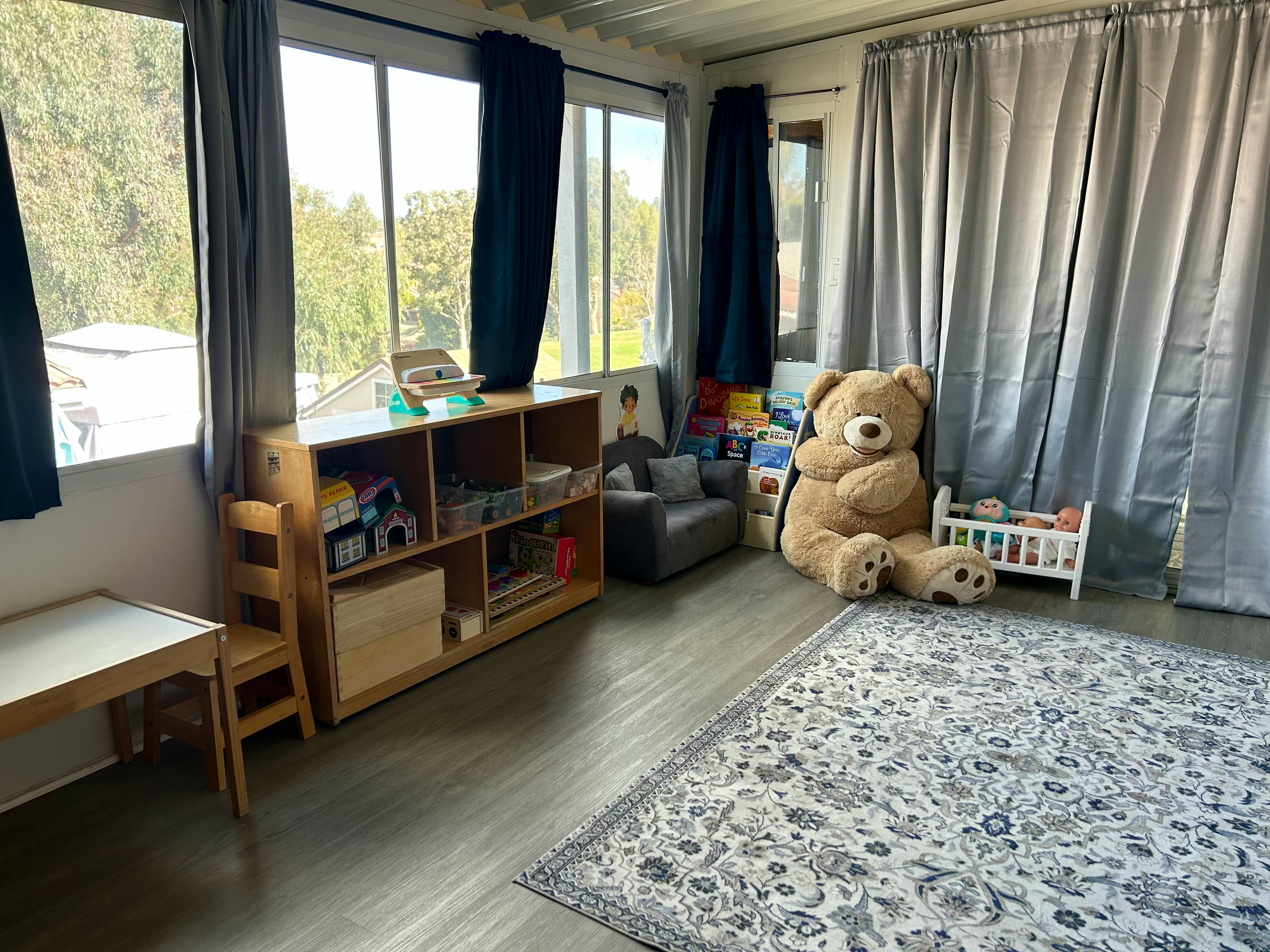 Playroom with large windows, a bookshelf, and a giant teddy bear