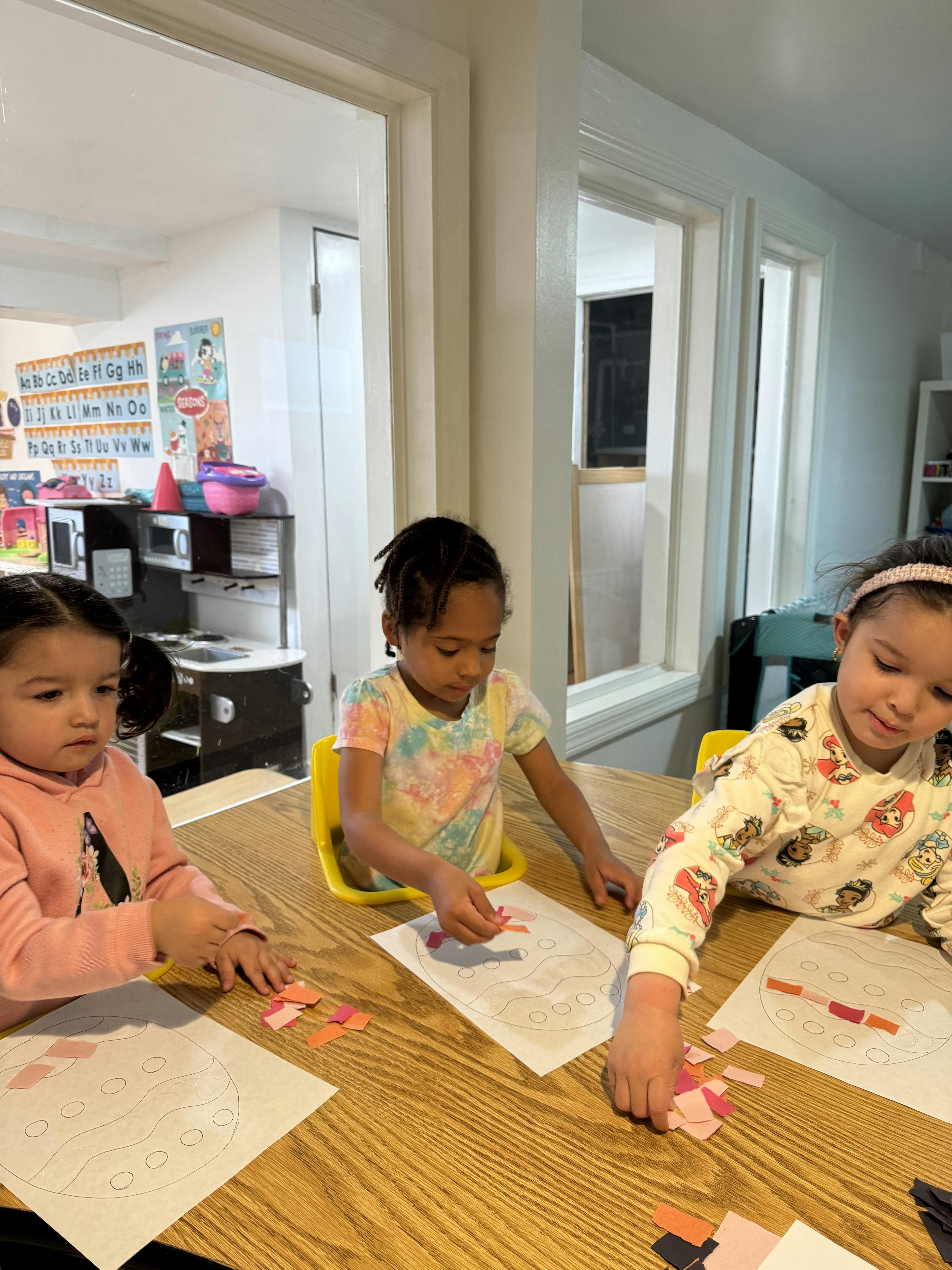 Three children sitting at a table doing crafts with paper crafts