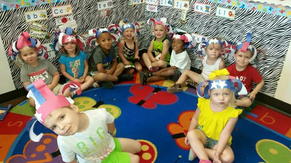 Group of children wearing paper hats sitting on a colorful rug