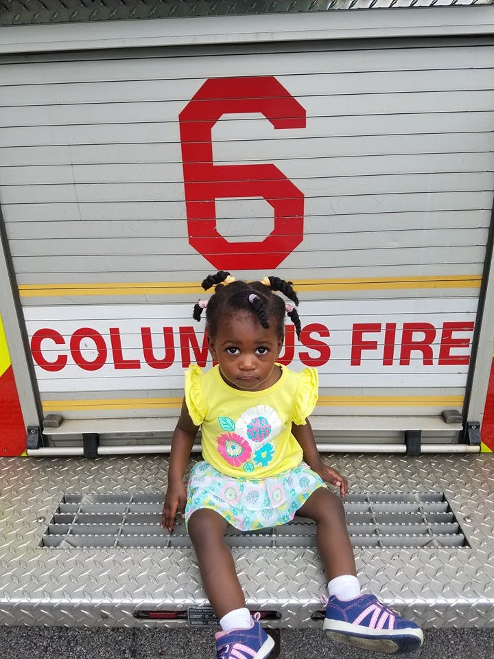 Child sitting in front of a fire truck with "COLUMBUS FIRE" and number 6