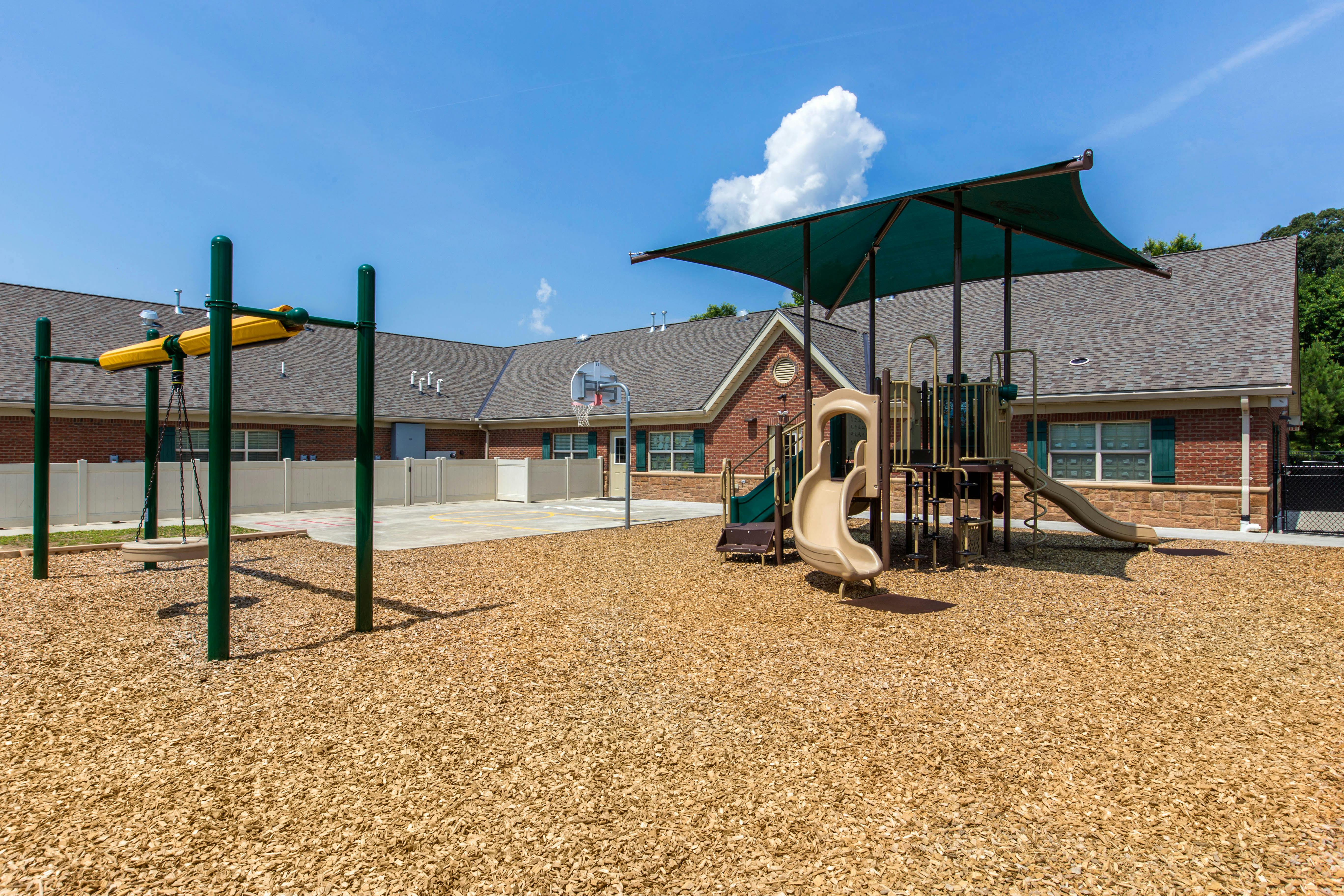 Playground with swings, slides, basketball hoop, and wood chip ground