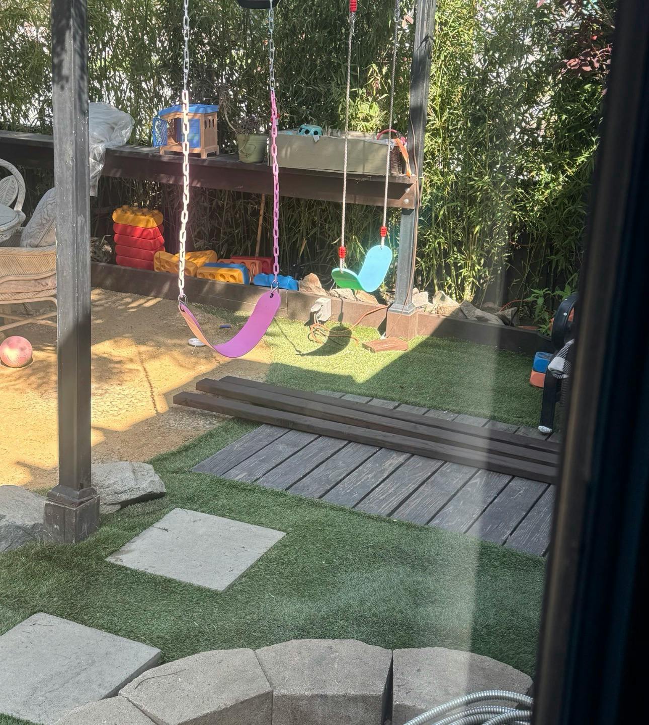Swingset in a backyard with green grass and bamboo in the background